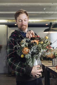 Man tweaking a flower arrangement in a silver vase