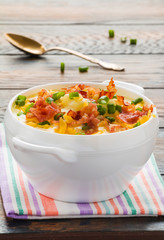 Loaded baked potato soup with crispy roasted bacon in a white bowl on the wooden rustic table.