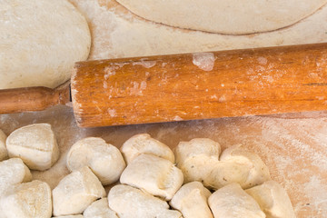 Fresh pizza dough with a rolling pin on a wooden table.