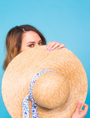Beautiful young woman wears in summer dress and straw hat is laughing on blue background with copy space