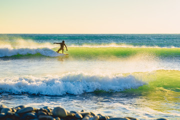 Surfer on green wave at sunset or sunrise. Surfer in ocean and waves