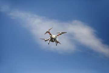 Fototapeta na wymiar White drone hovering in blue sky. Uav drone copter or quadrocopter flying with digital camera