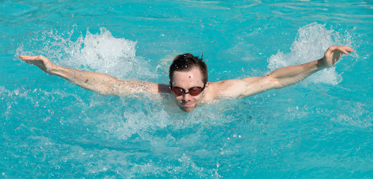 Young man with water goggles swim in a swimming pool, butterfly style