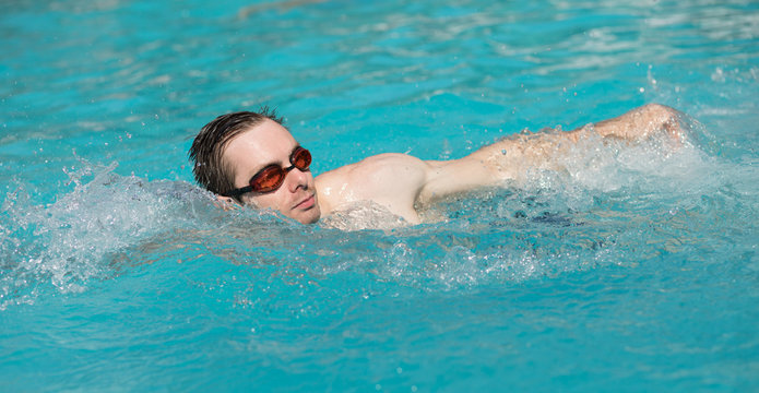 Young man with water goggles swim in a swimming pool, crawl style