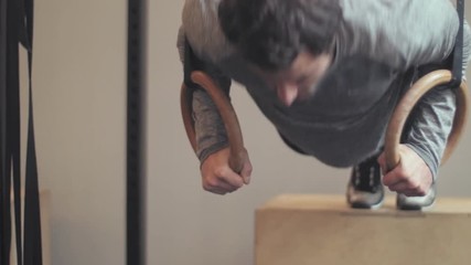 Fit man doing gymnastic ring press ups on a box in the gym