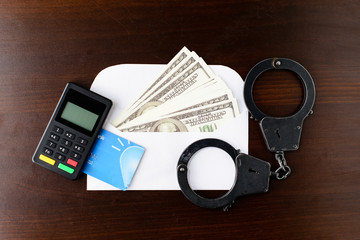steel police handcuffs, dollars money, payment device and bank card on wooden background, top view. Concept of illegal payment, bribery, venality, corruption and fraud