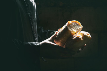 Loaf of fresh baked wheat bread in man's hands in sunshine. Rustic day light in dark room.