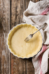 Dough for baking quiche tart in ceramic baking form ready for bake on kitchen towel over old plank...