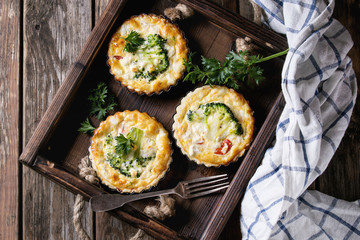 Baked homemade quiche pie in mini metal forms served with fresh greens, kitchen towel and fork in...