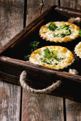 Baked homemade quiche pie in mini metal forms served with fresh greens in dark wood tray on old plank wooden background.