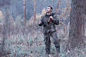 A man in camouflage and with a hunting rifle in a forest on a spring hunt