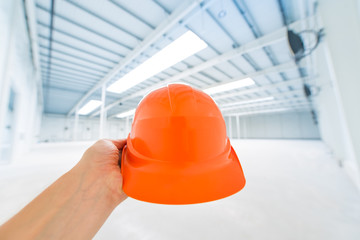 Kask ochronny na głowę trzymany w dłoni na hali produkcyjnej o stalowej konstrukcji