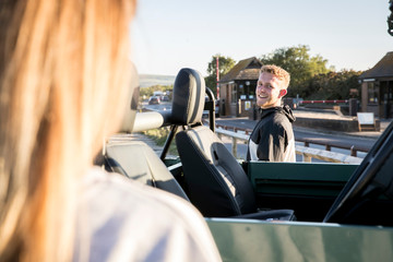Over shoulder view of young man and girlfriend with convertible four wheel drive at coastal carpark