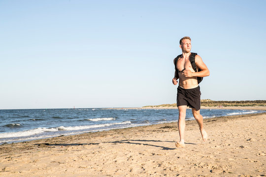 Young male runner wearing shorts and backpack running along beach