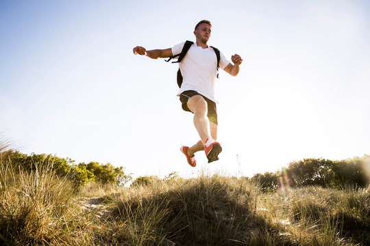 Young man training, jumping mid air from sand dunes