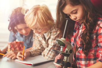 Attentive girl standing near microscope and looking through eyepiece
