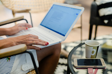 Close up of defocused businesswoman hand busy typing on laptop light background, drinking coffee. Top side view, copy space photography. Social connection network, communication technology