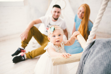 Obraz na płótnie Canvas A happy family of three. Mom, dad, child one year old girl in dress play, laugh, smile in bright room. Sunny