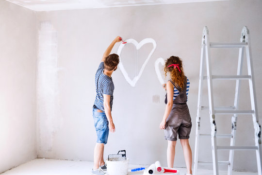 Couple painting heart on the wall in their house.