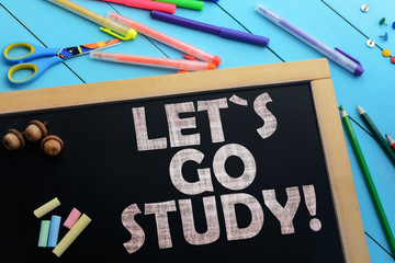 Text let`s go study on a black chalkboard on the table with school accessories (pens, pencils, brushes)