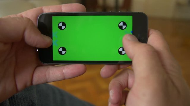 Smart Phone held by hands. Green screen Chroma Key. Close up. Tracking motion. Horizontal. Person sitting, telephone on the leg, blue jeans / pants. - . Swipe left / right animation.