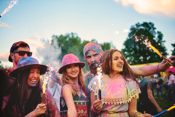 Young adults covered in coloured chalk powder dancing with sparklers at festival