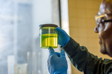 Lab technician inspecting beaker of yellow biofuel in biofuel plant laboratory