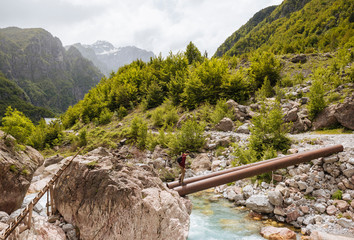 Man crossing waal river on bridge made of pipes, Accursed mountains, Theth, Shkoder, Albania, Europe