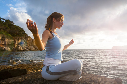 Woman sitting on rocks by sea meditating, Palma de Mallorca, Islas Baleares, Spain, Europe