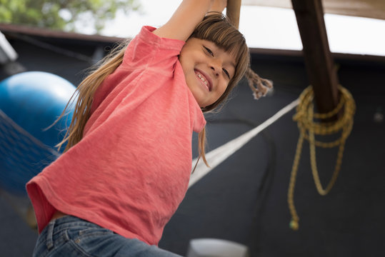 Girl hanging on monkey bar looking down at camera smiling