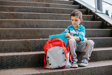 Unhappy young student sitting outside school and putting books in his school bag