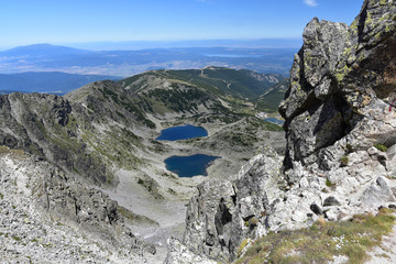 View from Mount Musala - the highest peak on Balkan Peninsula - down to the hiking trail, steep rocky slopes, lakes and huts. Bright summer day in Rila Mountains, Bulgaria