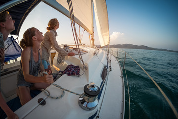 Three young women adjust the genoa sail after entering in a calm area of a tropical sea