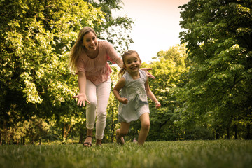 Fototapeta premium Mother and daughter running trough meadow. Mother chases her daughter.
