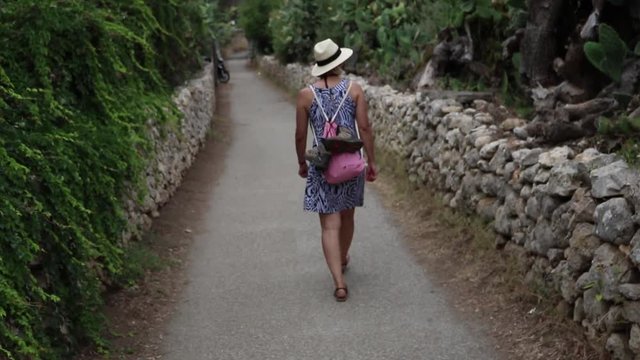 woman in summer dress is walking down a stonewalled way