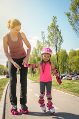 Mother and her little daughter inline skating on sidewalk. Mother and daughter enjoying in spring...