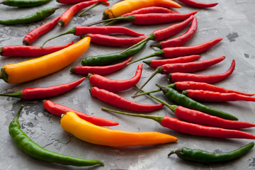 Assorted set of different colors hot chili peppers on grey marble stone surface. Mexican mix of green, yellow and red peppers, Cooking concept. Spicy kitchen ingredients.  Top view. Food background.
