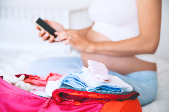 Pregnant woman packing for hospital and taking notes in smart phone