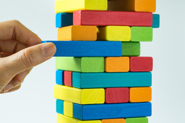 Hand pulling colorful wooden block from the tower in as Risk or stability concept