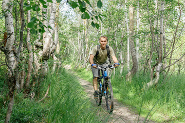 Naklejka premium a young man rides through a forest path on a bike