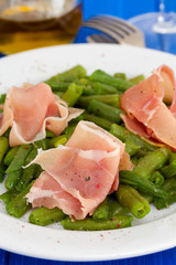 green beans with prosciutto on white plate on wooden background