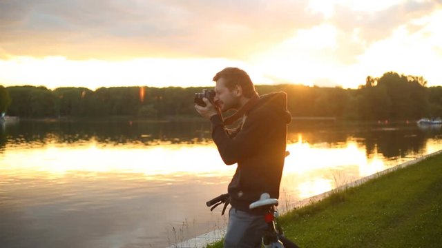 A young man came by bicycle to the shore of the lake and takes pictures of the sunset