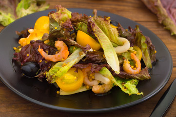 Fresh mix salad with shrimps, yellow cherry tomatoes and balsamic sauce. on wooden background. Close-up. Top view