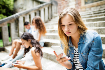 Teenage student girl with smart phone sitting on stone steps.