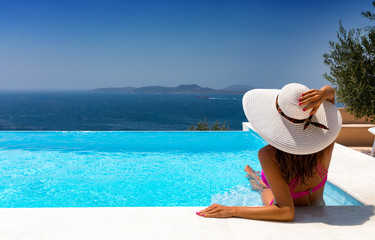 Fototapeta na wymiar Attraktive Frau mit weißem Hut entspannt in einem Infinity Pool