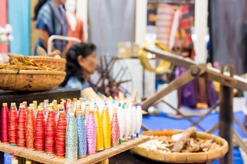 A closeup image of an old weaving Loom and thread of yarn with blurry picture of Woman weaving traditional instruments by hand background.