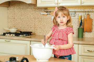 Cute little helper girl helping her mother cooking in a kitchen. Happy loving family are preparing bakery.