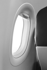 Gray aircraft window and backside of the passenger seat with black leather cover in the cabin crew, one airplane chair beside windowpane daylighting