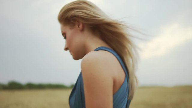 Closeup view of attractive young blond woman in a blue dress walking through golden wheat field. Freedom concept. Slowmotion shot