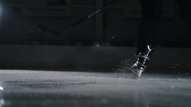 Hockey player make ice sparkles on high speed braking. Motion blur. Legs view only, hockey stick in hands, canadian tricks